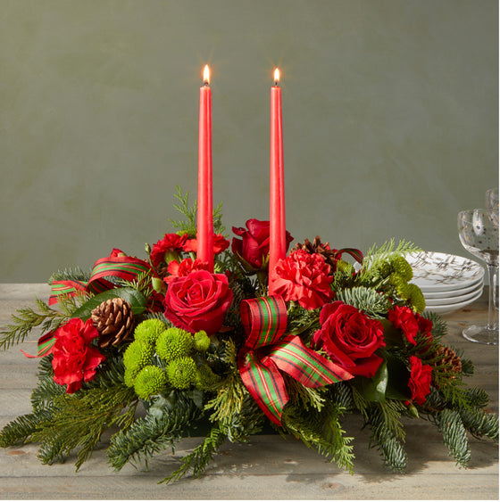 Decorative floral arrangement with red candles and ribbons on a wooden surface.