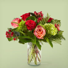  Bouquet of red and pink roses with greenery and berries in a clear vase on a light green background
