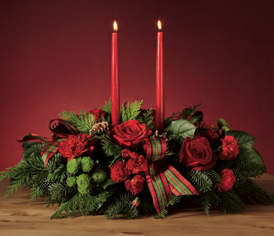 Decorative floral arrangement with red candles on a wooden surface against a red background